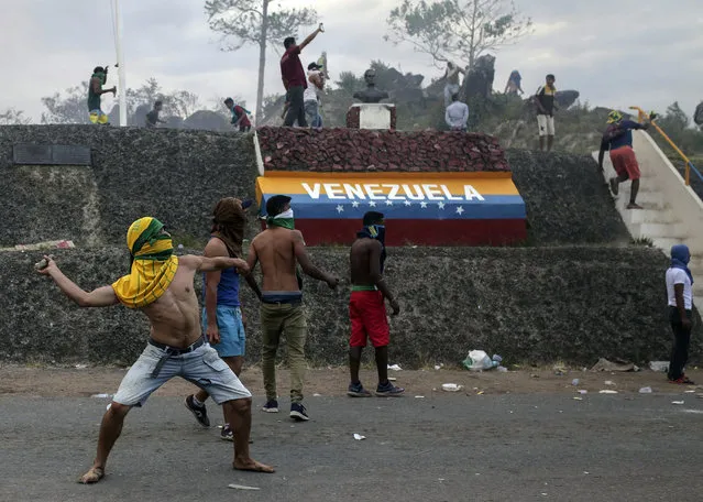 Venezuelan demonstrators throw stones during clashes with authorities, at the border between Brazil and Venezuela, Saturday, February 23, 2019. Tensions are running high in the Brazilian border city of Pacaraima. Thousands remained at the city's international border crossing with Venezuela to demand the entry of food and medicine. (Photo by Ivan Valencia/AP Photo)