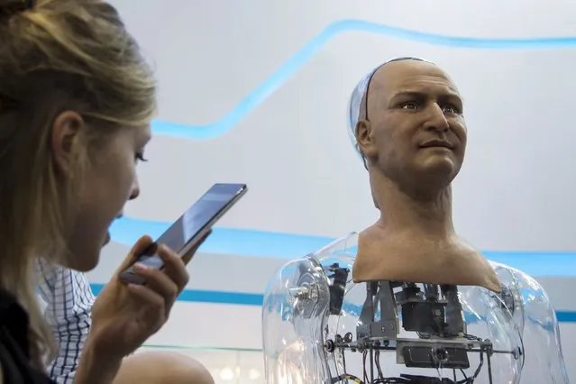 A staff talks to a humanoid robot named Han developed by Hanson Robotics via a mobile phone during the Global Sources spring electronics show in Hong Kong April 18, 2015. According to Hanson Robotics the robot's skin is made out of a material called Frubber, an elastic polymer that mimics the human skin, and installed with about 40 motors on its face which help create various expressions. Han can answer simple questions and staff said it can be used in the field of customer service. (Photo by Tyrone Siu/Reuters)