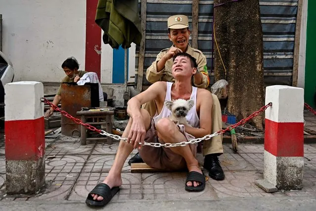 A man removes white hair for his friend in Hanoi street on January 18, 2024. (Photo by Nhac Nguyen/AFP Photo)