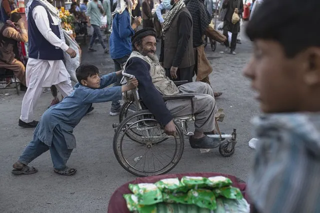A boy pushes a man in a wheelchair trough a market in Kabul, Afghanistan, Tuesday, October 12, 2021. (Photo by Ahmad Halabisaz/AP Photo)