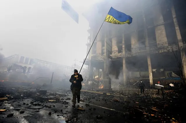 An anti-government protester holds a Ukranian flag as he advances through burning barricades in Kiev's Independence Square February 20, 2014. (Photo by Yannis Behrakis/Reuters)