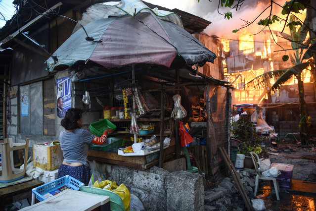 A resident gathers her goods for sale, while a house nearby burns after a fire gutted an informal settlers area in Quezon City suburban Manila on March 20, 2019. Local news reported some 250 houses were destroyed leaving 750 families homeless. (Photo by Ted Aljibe/AFP Photo)