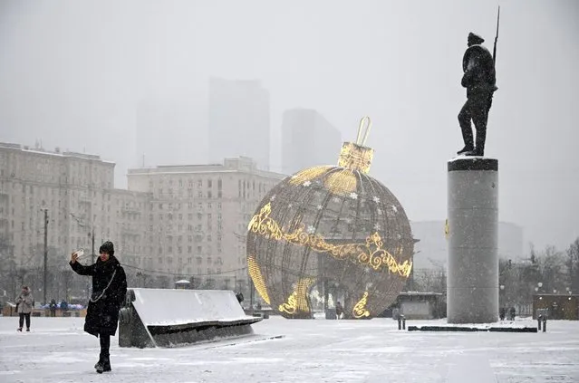A woman makes a selfie photo next to Christmas decorations and a Monument to the Heroes of the WWI at the Poklonnaya Hill in western Moscow on December 13, 2021. (Photo by Alexander Nemenov/AFP Photo)