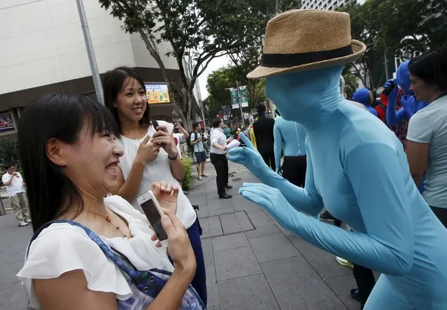 Japanese passer-bys are greeted by a participant wearing Zentai costume, or skin-tight bodysuit from head to toe, in a march down the shopping district of Orchard Road during Zentai Art Festival in Singapore May 23, 2015. (Photo by Edgar Su/Reuters)