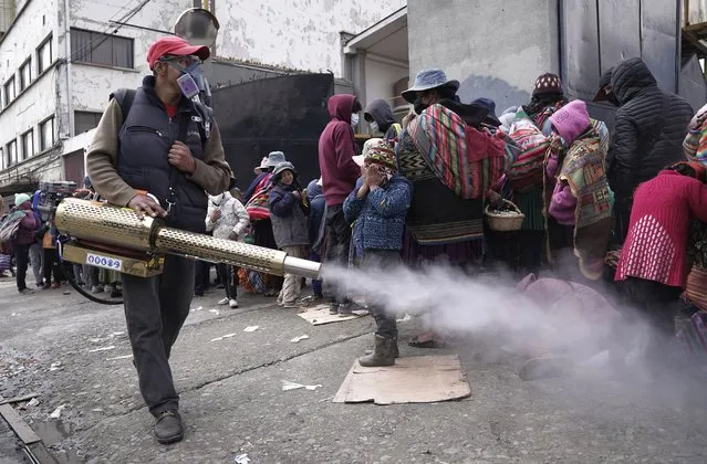 A worker sprays disinfectant around people who traveled from the provinces to Monte de Oración church for donated food and clothing during the church's annual Good Samaritan campaign in La Paz, Bolivia, Tuesday, December 28, 2021. Due to the COVID-19 pandemic, the church is distributing the goods outdoors. (Photo by Freddy Barragan/AP Photo)