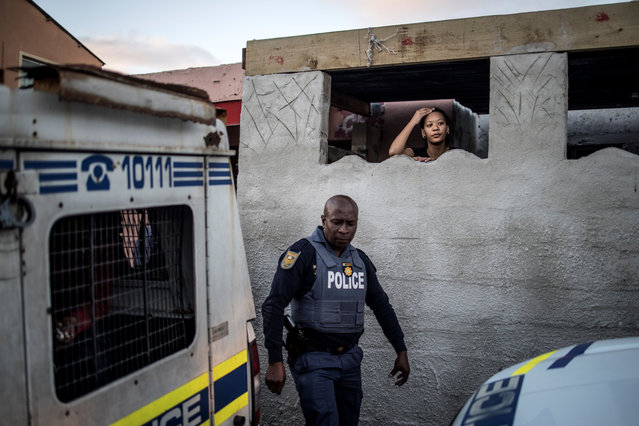 The relative of a man detained in a police van looks on as South African policeman leaves their residence during a joint police operation in the Mitchel's Plan district of the Cape Flat in Cape Town, on August 9, 2019. A total of 1320 South Africa National Defence Forces service members have been deployed to Cape Town's gang-ridden areas to support police operations to prevent and combat crime. (Photo by Marco Longari/AFP Photo)