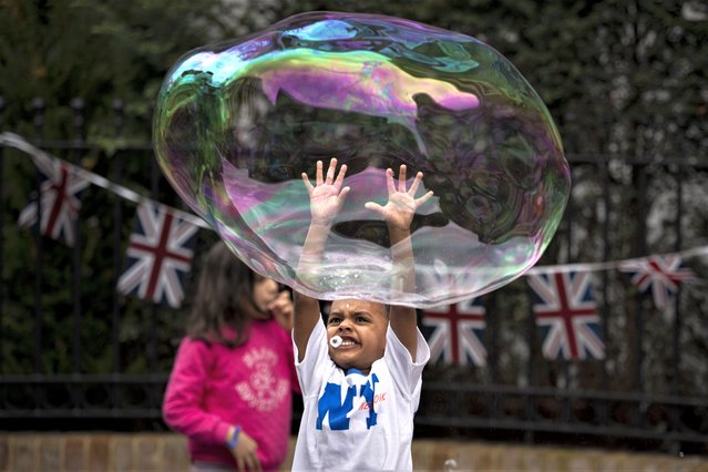 A child jumps to pop a soap bubble during the Big Lunch celebrations on Holland Street in London, Sunday, May 7, 2023. The Big Lunch is part of the weekend of celebrations for the Coronation of King Charles III. (Photo by Andreea Alexandru/AP Photo)