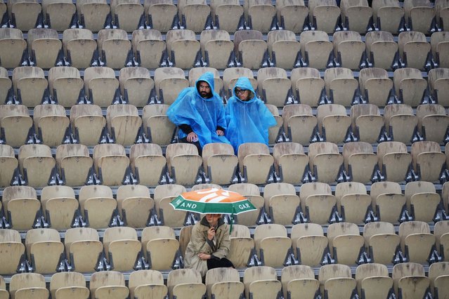 Spectators sit in the tribunes with rain clothes and an umbrella on day seven of the French Open tennis tournament at the Roland Garros Complex in Paris on June 1, 2024. (Photo by Dimitar Dilkoff/AFP Photo)