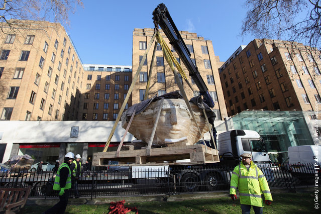 Workmen use a crane to winch a large stone head, created by British sculptor Emily Young, into Berkeley Square