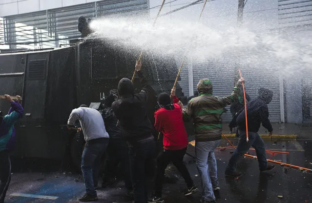 Hooded protesters attack a police water canon near Congress where President Michelle Bachelet was presenting the state-of-the-nation report, in Valparaiso, Chile, Saturday, May 21, 2016. The anti-government protest began as a peaceful march but turned rough as some demonstrators threw rocks at police and gasoline bombs at buildings, resulting in the death of one man who reportedly died of asphyxiation. (AP Photo/Esteban Felix)