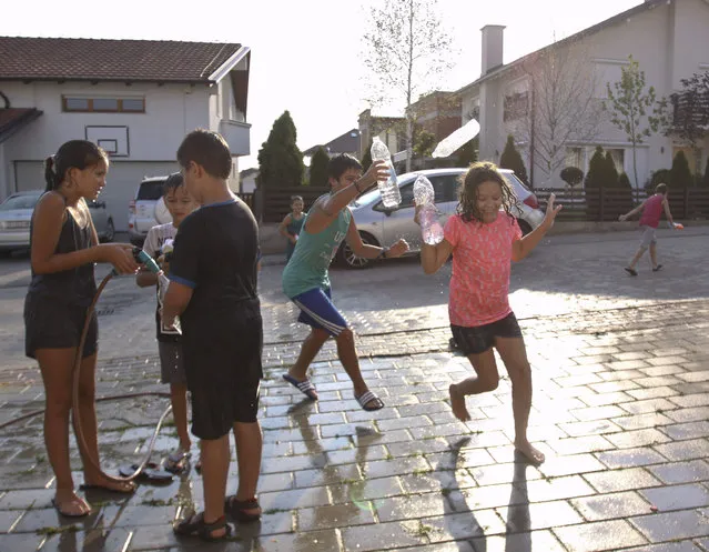 Kids throw water at each other as they try to refresh themselves on a hot day in Hajvali 15 km (12 miles) from capital Pristina on Sunday, July 19, 2015. Europe's heat wave has pushed the mercury to levels as high as 40 degrees Celsius, 104 fahrenheit. (Photo by Visar Kryeziu/AP Photo)