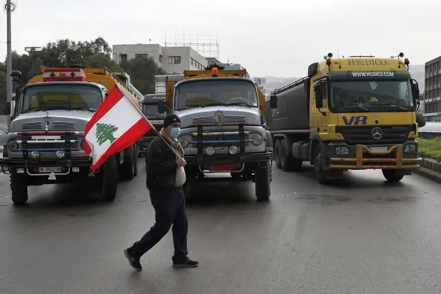 A truck driver holds a Lebanese flag as others drivers block a main highway with their vehicles during a general strike by public transport and workers unions paralyzed Lebanon in protest to the country's deteriorating economic and financial conditions, in Beirut, Lebanon, Thursday, January 13, 2022. (Photo by Bilal Hussein/AP Photo)