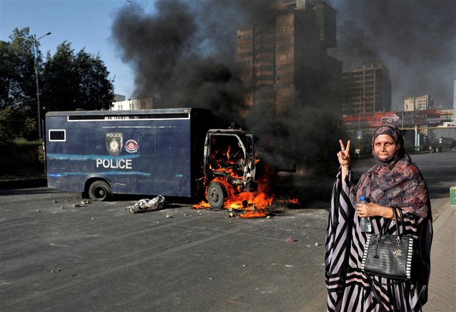 A woman gestures next to a burning police vehicle during a protest by the supporters of Pakistan's former Prime Minister Imran Khan after his arrest, in Karachi, Pakistan on May 9, 2023. The opposition party of Pakistan's former Prime Minister Khan called for demonstrators to remain peaceful, hours after mobs angered over the dramatic mid-trial arrest set fire to the residence of a top army general in the eastern city of Lahore. (Photo by Akhtar Soomro/Reuters)