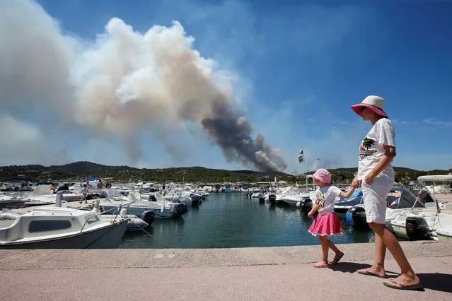 A woman and her daughter walk near leisure boats in a port as a plume of smoke from burning fires  fills the sky in Bormes-les-Mimosas, in the Var department, France, July 26, 2017. (Photo by Jean-Paul Pelissier/Reuters)
