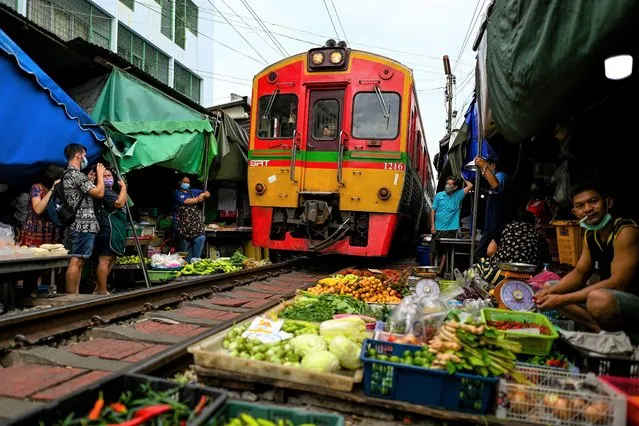 This photograph taken on June 4, 2022 shows a passenger train passing through the Mae Klong railway market in Samut Songkhram province, around 80 kms (50 miles) southwest of Bangkok. (Photo by Manan Vatsyayana/AFP Photo)