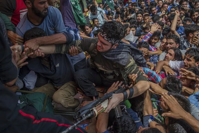 Villagers help a Kashmiri militant to climb on a stage as he appears in a funeral to pay tributes to slain rebel Suhail Ahmed, who was killed in an ambush by Indian government forces in Tantraypora, some 85 kilometers (53 miles) south of Srinagar, Indian controlled Kashmir, Thursday, August 3, 2017. A pair of ambushes by Indian government forces and Kashmiri rebels early Thursday killed two soldiers and two militants in the disputed Himalayan region. At least two militants appeared at the funeral and fired dozens of rounds in honor of their fallen comrades. (Photo by Dar Yasin/AP Photo)