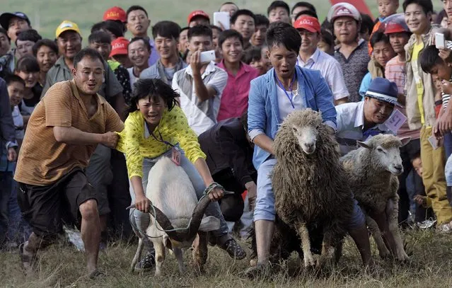 People look on as participants ride goats and sheep during a race to celebrate a local festival in Fengshan town, Guizhou province July 26, 2014. (Photo by Reuters/China Daily)