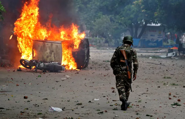 A member of the security forces walks towards a burning vehicles during violence in Panchkula, India, August 25, 2017. (Photo by Cathal McNaughton/Reuters)