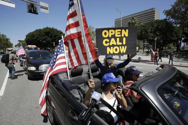 Protesters drive by in a convertible car during a rally calling for an end to California Gov. Gavin Newsom's stay-at-home orders amid the COVID-19 pandemic, Wednesday, April 22, 2020, outside of City Hall in downtown Los Angeles. (Photo by Marcio Jose Sanchez/AP Photo)