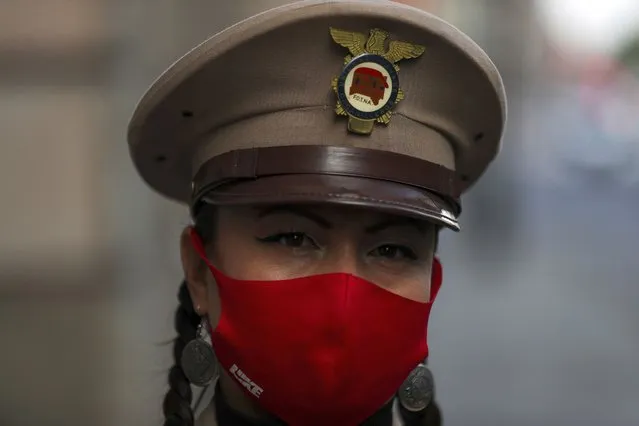 An organ grinder, wearing a protective face mask, eyes the camera as she waits for a delivery of donated groceries, in Mexico City, Thursday, June 4, 2020. CADENA, a non-profit organization dedicated to assisting during emergencies and disasters around the world, dispatched groceries to hundreds of organ grinders who play for tips from passersby but have lost their source of income due to restrictions amid the new coronavirus. (Photo by Fernando Llano/AP Photo)