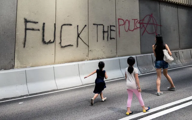 A woman and two girls walk past graffiti “f*ck the police” on a highway barricaded off to traffic by pro-democracy protestors in Hong Kong on October 1, 2014. Hong Kong has been plunged into the worst political crisis since its 1997 handover as pro-democracy activists take over the streets following China's refusal to grant citizens full universal suffrage. (Photo by Alex Ogle/AFP Photo)