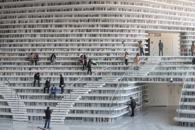 This picture taken on November 14, 2017 shows people visiting the Tianjin Binhai Library. A futuristic Chinese library has wowed book lovers around the world with its white, undulating shelves rising from floor to ceiling, but if you read between the lines you'll spot one problem. Those rows upon rows of book spines are mostly images printed on the aluminium plates that make up the backs of shelves. (Photo by Fred Dufour/AFP Photo)