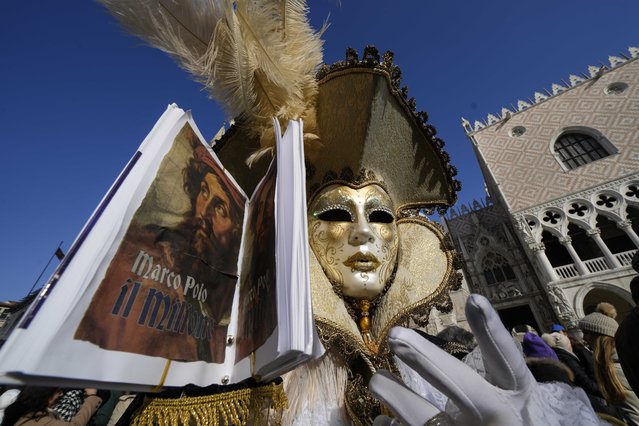 A man wears a mask and holds the replica a the book “The Million” a report of Marco Polo's travels in Asia, during the Carnival in Venice, Italy, Sunday January 28, 2024. Venice is marking the 700th anniversary of the death of Marco Polo with a yearlong series of commemorations, starting with the opening of Carnival season honoring one of the lagoon city's most illustrious native sons. (Photo by Luca Bruno/AP Photo)