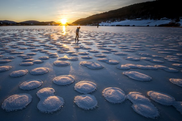 A skater observes pancakes snow on the frozen Lake des Rousses in Les Rousses, central-eastern France, on January 1, 2025. This phenomenon forms when slushy ice in water clumps into round, pancake-like shapes due to waves or currents. (Photo by Fabrice Coffrini/AFP Photo)