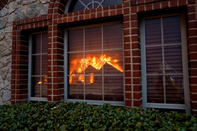 Reflection of a residence burning is pictured on glass panes during a wildfire in Stillwater, Oklahoma, on March 14, 2025. (Photo by Nick Oxford/Reuters)