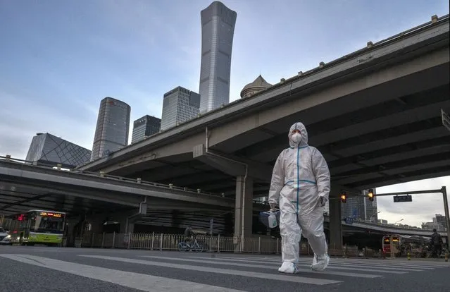 An epidemic control worker is dressed in protective equipment to protect against the spread of COVID-19 as he walks across a road in the Central Business District, after most workers were expected to work from home, on November 21, 2022 in Beijing, China. In an effort to try to bring rising cases under control, the local government on Friday closed many restaurants for inside dining, switched  schools to online studies, and asked people to work from home. Though the government recently revised its COVID strategy, it has said it will continue to stick to its strict zero tolerance policy with mandatory testings, quarantines and lockdowns in many areas in an effort to control the spread of the virus. (Photo by Kevin Frayer/Getty Images)