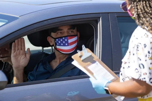 A U.S. immigration officer administers the oath to Palestinian Omar Abdalla during a swearing-in of newly naturalized United States citizens in an empty parking lot during the outbreak of the coronavirus disease (COVID-19) in Santa Ana, California, U.S., July 29, 2020. (Photo by Mike Blake/Reuters)