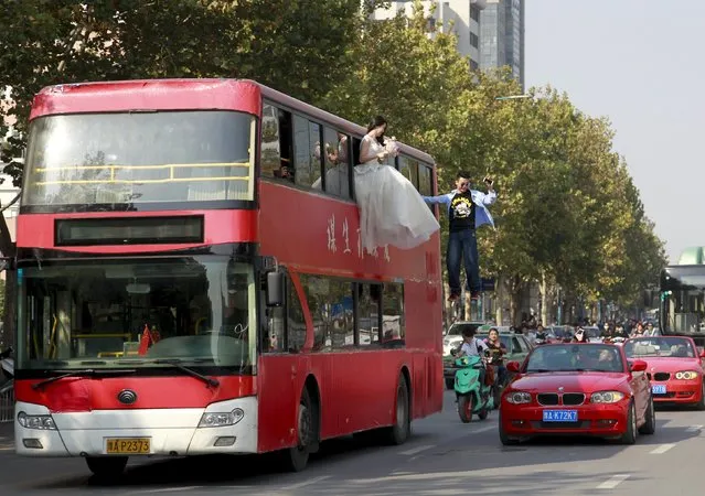 Magician Lei Xin (C) is seen suspended outside a double-deck bus, next to a woman in a wedding gown, as they participate in a performance on a street in Zhengzhou, Henan province, China, October 15, 2015. According to local media, the performance, organized by Lei and his friends, is aiming to promote a healthier view of love and marriage among young people. (Photo by Reuters/Stringer)