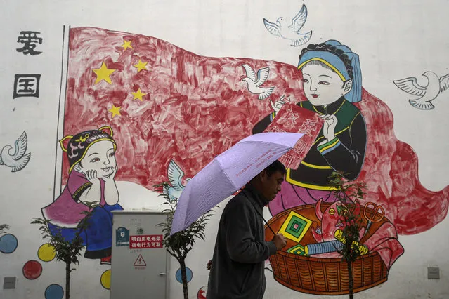 A man holding an umbrella walks by a new village house decorated with a patriotic painting which was built by the Chinese government for ethnic minority members in Ganluo county, southwest China's Sichuan province on September 10, 2020. (Photo by Andy Wong/AP Photo)