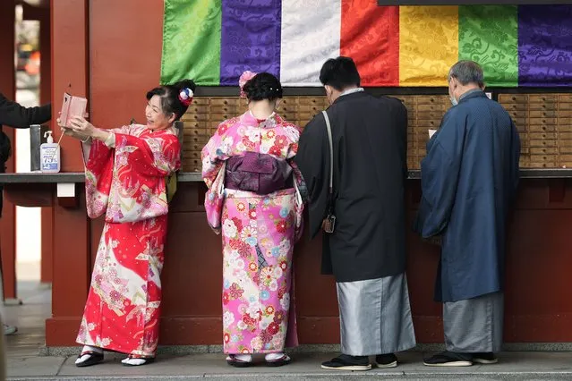 A group of tourists from Singapore in Japan's traditional kimono attire buy fortune paper as one of them takes a selfie at Sensoji Buddhist temple in Tokyo, Friday, January 13, 2023. (Photo by Hiro Komae/AP Photo)