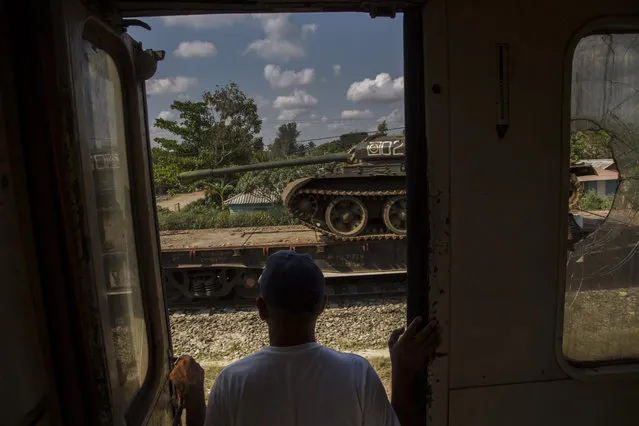 In this March 23, 2015 photo, a man looks at a tank being transported on a paused cargo train, as he travels by train through the province of Holguin, Cuba. The train system suffered along with much of the country's infrastructure when the Soviet Union's collapse cut Cuba off from the subsidies that Moscow had pumped into its economy. Currently, a longstanding U.S. trade embargo makes it hard to get parts. (Photo by Ramon Espinosa/AP Photo)