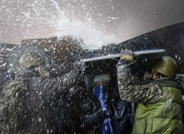 Pro-European integration protesters take cover from water sprayed from a fire engine at the site of clashes with riot police in Kiev, in this January 23, 2014 file photo. (Photo by Vasily Fedosenko/Reuters)