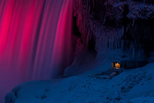 An observation point at the base of Niagara Falls in Niagara Falls, Ontario, is covered in ice as the falls are illuminated by colored light on January 9, 2018. A giant winter “bomb cyclone” walloped the US East Coast on January 5, 2018, with heavy snow and freezing cold that made for treacherous travel conditions and bone- chilling misery. (Photo by Geoff Robins/AFP Photo)