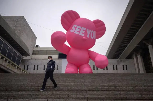 A man wearing a face mask walks down steps before an inflatable bear outside the Sejong theatre in central Seoul on December 10, 2020. (Photo by Ed Jones/AFP Photo)