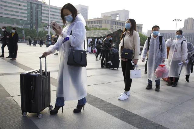 Passengers wearing face masks and rain coats to protect against the spread of new coronavirus gather outside of Hankou train station after of the resumption of train services in Wuhan in central China's Hubei Province, Wednesday, April 8, 2020. After 11 weeks of lockdown, the first train departed Wednesday morning from a re-opened Wuhan, the origin point for the coronavirus pandemic, as residents once again were allowed to travel in and out of the sprawling central Chinese city. (Photo by Ng Han Guan/AP Photo)