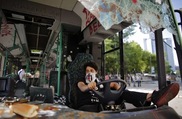 A Besiktas soccer fan uses his team's scarf as a mask while sitting in a damaged bus at Taksim Square in central Istanbul June 4, 2013. Days of anti-government protest in Turkey have achieved one feat that has eluded the authorities for years: uniting the fiercely rival and sometimes violent supporters of Istanbul's “Big Three” football clubs. Besiktas, Galatasaray and Fenerbahce fans have come together in new-found solidarity during five days of demonstrations against Prime Minister Tayyip Erdogan's government. (Photo by Murad Sezer/Reuters)