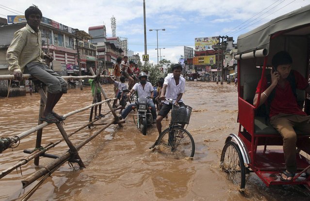 People move through a waterlogged street in Gauhati, India, Tuesday, July 16, 2013.  Heavy showers flooded some areas in the city on Tuesday. (Photo by Anupam Nath/AP Photo)
