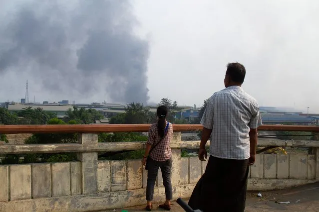 People look at smoke believed to be from a factory fire after Chinese-financed factories were set ablaze in the poor, industrial suburb of Yangon during the security force crack down on anti-coup protesters at Hlaingthaya, Myanmar on March 14, 2021. (Photo by Reuters/Stringer)