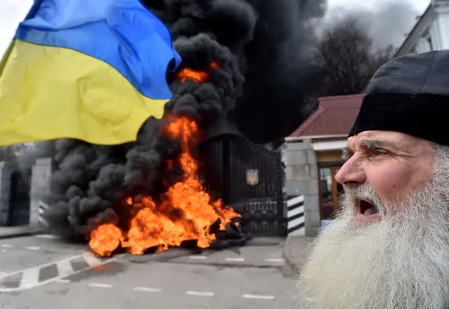An elderly Orthodox priest shouts as fighters of the “Aydar” Ukrainian volunteer battalion, burn tyres at the entrance to the Ukrainian Defence Ministry in Kiev, on February 2, 2015 during an action to prevent the possible disbandment of their battalion. (Photo by Sergei Supinsky/AFP Photo)