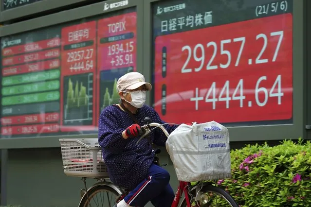 A woman wearing a protective mask rides a bicycle in front of an electronic stock board showing Japan's Nikkei 225 index at a securities firm Thursday, May 6, 2021, in Tokyo. Asian shares were mixed Thursday on cautious optimism about upcoming company earnings reports showing some recovery from the damage of the coronavirus pandemic. (Photo by Eugene Hoshiko/AP Photo)
