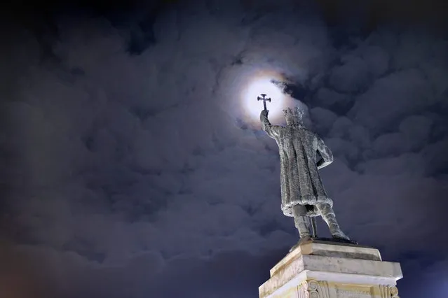 The light reflected by the full moon breaks through the clouds behind the statue of “Stephen the Great” near the government headquarters in Chisinau, Moldova, late 23 January 2016. Chisinau saw a quiet Saturday without further protests following days of clashes in the country's capital. Supporters of the politic platform “Demnitate si Adevar” (lit. Dignity and Truth), the Socialists and the “Our Party” party anounced a new protest against the new government on 24 January. “Stephen the Great” (1433-1504) was Prince of the Principality of Moldavia between 1457 and 1504. (Photo by Robert Ghement/EPA)