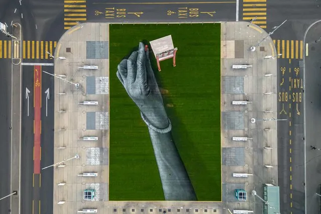 An aerial photograph taken on September 11, 2023 shows a giant biodegradable land art painting by French artist Guillaume Legros, aka Saype, representing a hand fixing the fourth leg to the “Broken Chair” a monumental wood sculpture installed in front of the Palace of Nations, which houses the United Nations offices in Geneva. The 12-meter-high “Broken Chair” commissioned by the NGO Handicap International symbolises the opposition to land mines and cluster bombs, and acts as a reminder to politicians and diplomats visiting Geneva. (Photo by Fabrice Coffrini/AFP Photo)