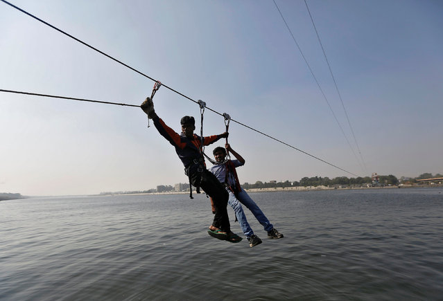 A worker (L) helps a man after he got stuck on a zip-line over the Sabarmati river on a sunny winter afternoon in Ahmedabad, India, December 26, 2016. (Photo by Amit Dave/Reuters)