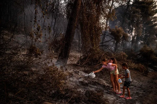 Children pour water after a forest fire near in the village of Kastri on Evia (Euboea) island, on August 10, 2021. Nearly 900 firefighters, reinforced overnight with fresh arrivals from abroad, were deployed on the country's second largest island as major towns and resorts remained under threat from a fire that has been burning for eight days. (Photo by Angelos Tzortzinis/AFP Photo)