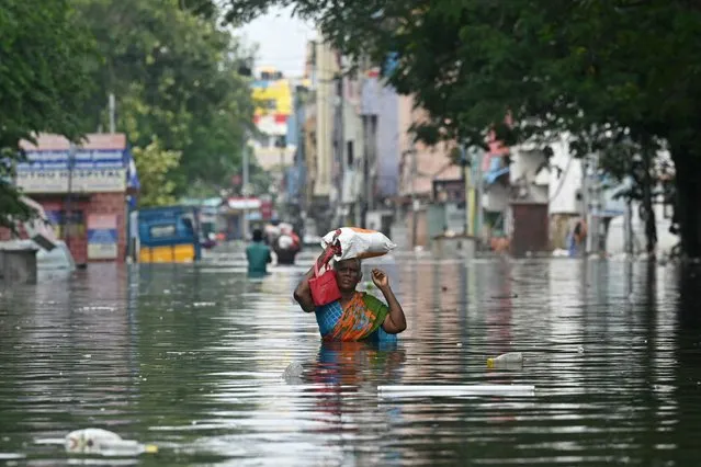 A woman along with her belongings, wades through a flooded street after heavy rains in Chennai on December 6, 2023. Chest-high water surged down the streets of India's southern city Chennai on December 5, with eight people killed in intense floods as Cyclone Michaung made landfall on the southeast coast. (Photo by AFP Photo/Stringer)