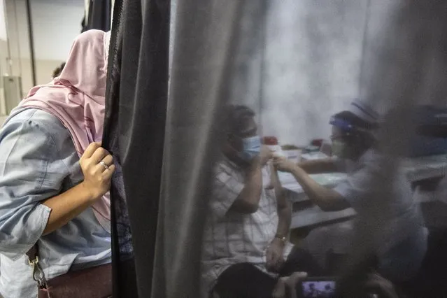 A woman watches on as her father receives a dose of COVID-19 vaccine at a vaccination centre in Kuala Lumpur, Malaysia, 31 May 2021. Malaysia International Trade and Exhibition Centre (MITEC) building has turned into a mega Covid-19 vaccination centre that can be expanded to handle 8,000 recipients daily when needed. (Photo by Ahmad Yusni/EPA/EFE)